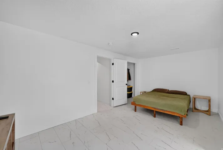 White walls with a recessed ceiling light, marble-look tile flooring, and a white interior door