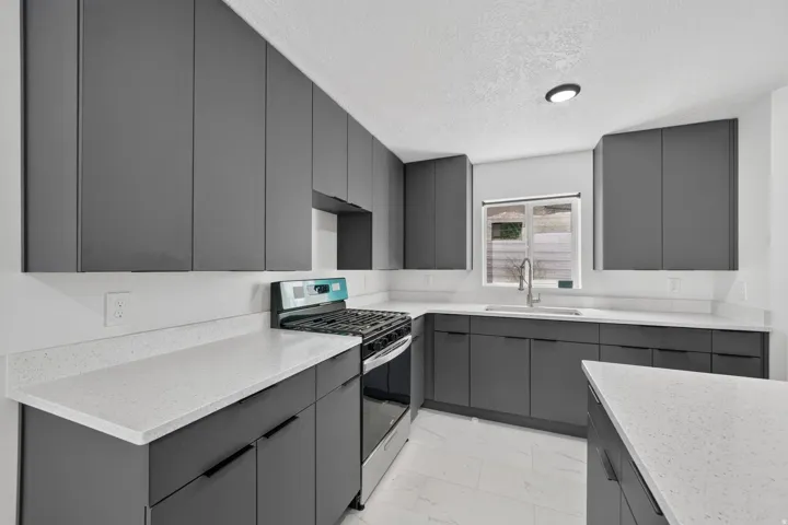 Modern kitchen featuring dark cabinetry, light countertops, a stainless steel range, a stainless steel sink with a gooseneck faucet, and white tile flooring