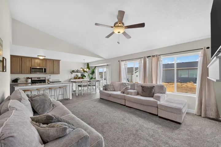 Vaulted ceiling with an integrated ceiling fan, large windows, wood-finish flooring, light-toned cabinetry, and stainless steel appliances