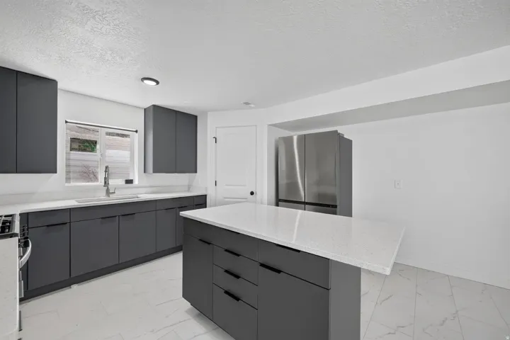 Sleek dark cabinetry with integrated hardware, light-toned countertops, and a stainless steel refrigerator