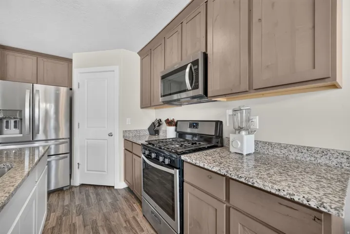 Kitchen featuring stainless steel appliances, wood-finish flooring, granite countertops, and light-toned cabinetry