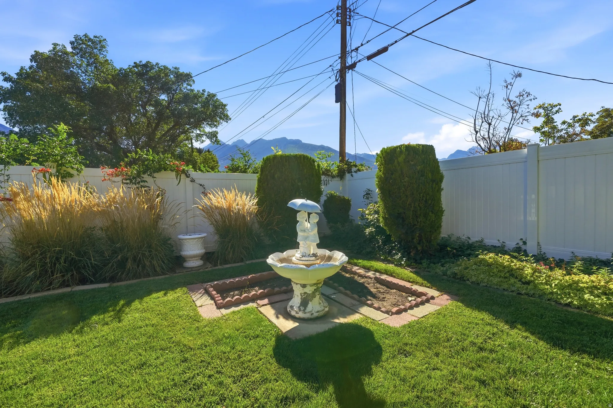 Landscaped yard featuring a decorative fountain, manicured lawn, and privacy fencing