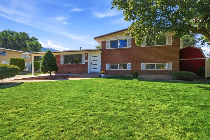 Brick exterior featuring white window shutters, a carport, and an expansive lawn