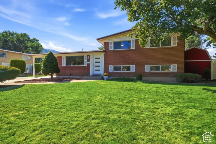 Brick exterior featuring white window shutters, a carport, and an expansive lawn