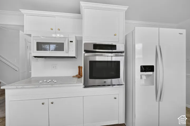 White cabinetry with crown molding, stainless steel built-in oven, built-in microwave, and a smooth cooktop