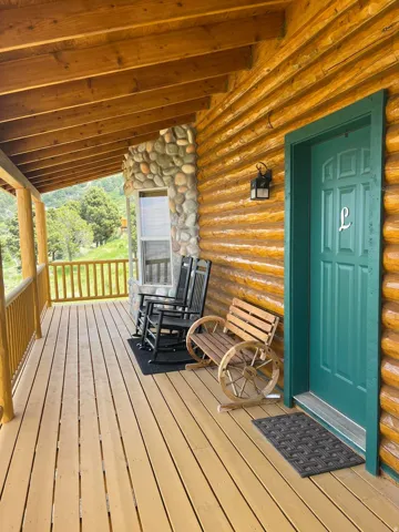 Expansive covered porch featuring a log exterior, natural wood ceiling, wood plank flooring, and a stone accent wall