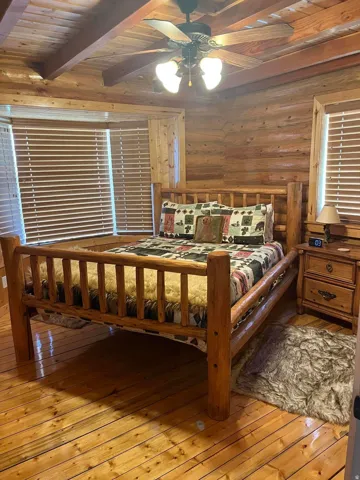 Wood-paneled walls and ceiling with exposed beams, wood-finish flooring, and a ceiling fan with integrated lighting