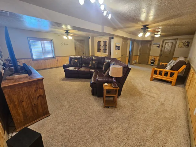 Recessed lighting and ceiling fans illuminate a carpeted room with wood-paneled wainscoting