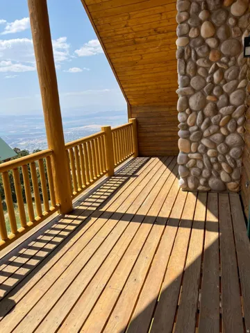 Expansive wood deck with a natural wood railing, a robust round log structural post, and a stone-clad exterior wall