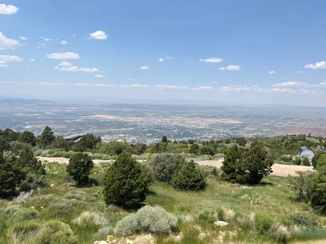 Expansive terrain with natural ground cover, distant cityscape, and surrounding mountain ranges