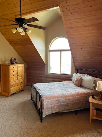 Vaulted ceiling with wood paneling, arched window, log-style wall, and carpet flooring