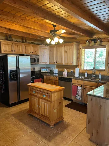Wood-paneled ceilings with exposed beams, stainless steel appliances, a built-in kitchen island, and a tile floor