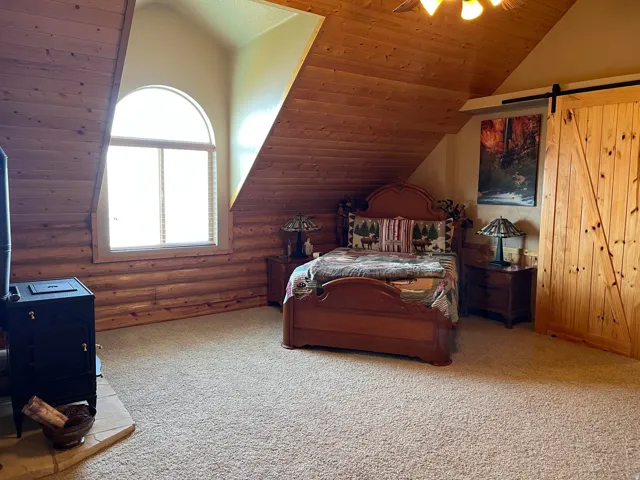 Natural wood walls and ceiling, arched window, wood-burning stove with stone hearth, and a wood barn door