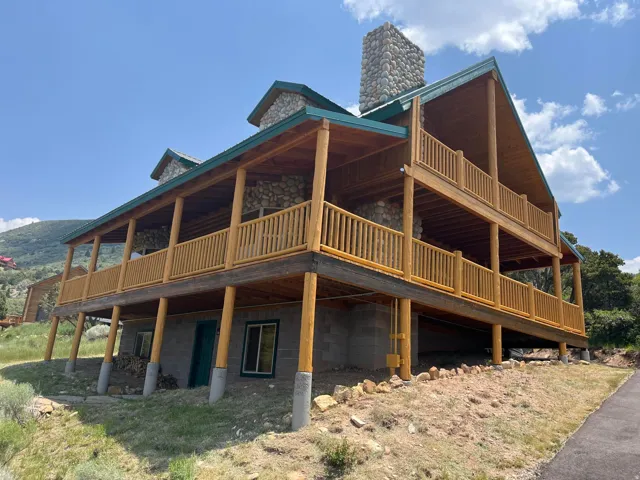 Two-story wood-finish wrap-around porch with stone exterior accents and a prominent stone chimney