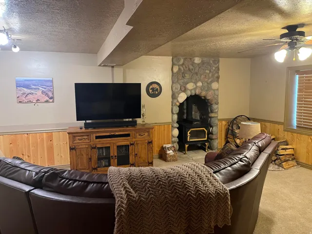 Stone-surround wood-burning stove with a hearth, wood paneling, ceiling fan with integrated lighting, and recessed ceiling lighting