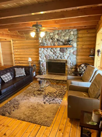 Stone fireplace with a wood mantle, exposed wood beam ceiling, wood plank walls, and wood-finish flooring