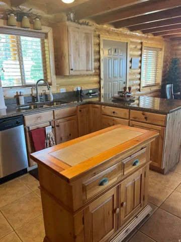 Kitchen featuring log wall construction, natural wood cabinetry, granite-style countertops, tile flooring, and a portable island with a tile insert