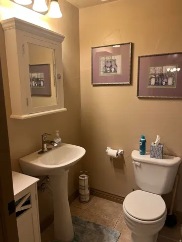 Pedestal sink with chrome faucet, wall-mounted medicine cabinet, toilet, and tiled flooring