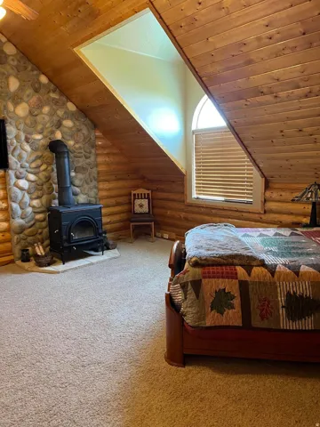 Wood-paneled sloped ceiling, exposed log walls, stone hearth, and an arched window