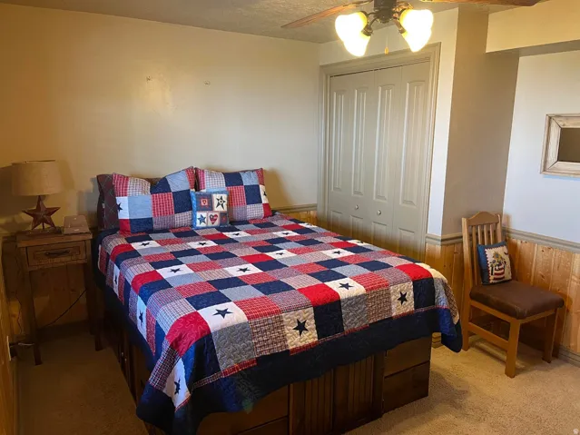 Bedroom featuring wood paneling, wall-to-wall carpeting, bi-fold closet doors, and a ceiling fan with integrated lighting