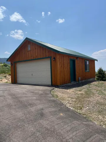 Modern garage structure featuring warm wood-finish exterior siding, a sectional overhead garage door, standing-seam metal roof, and multiple windows for natural light