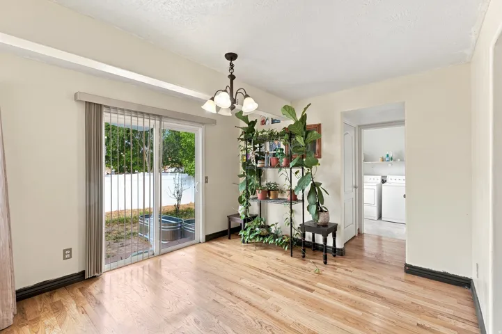 Hardwood flooring, sliding glass door, overhead chandelier, white walls, and a utility room featuring a washer and dryer