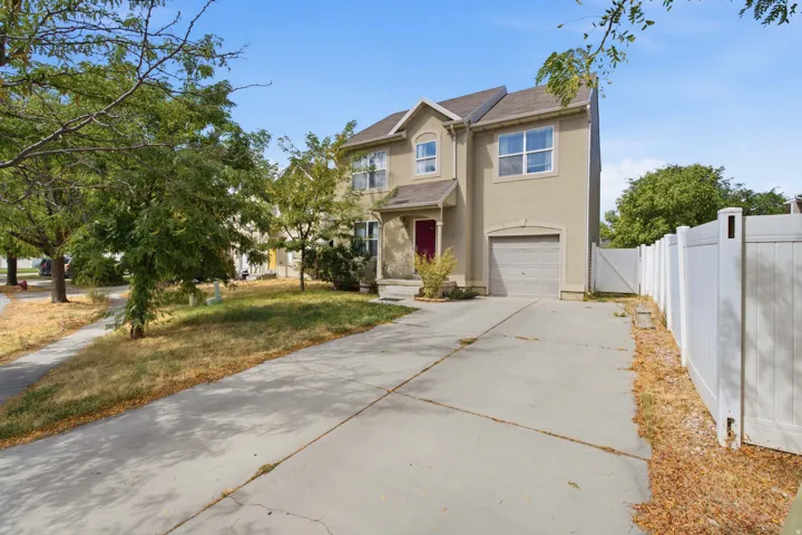Two-story stucco exterior with an attached garage, a concrete driveway, and a white fence