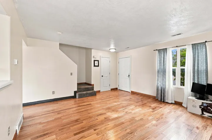 Wood-finish flooring throughout, bright window with natural light, and a carpeted staircase