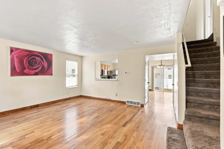 Expansive living area featuring wood-finish flooring, a pass-through window, and a staircase with carpeted treads
