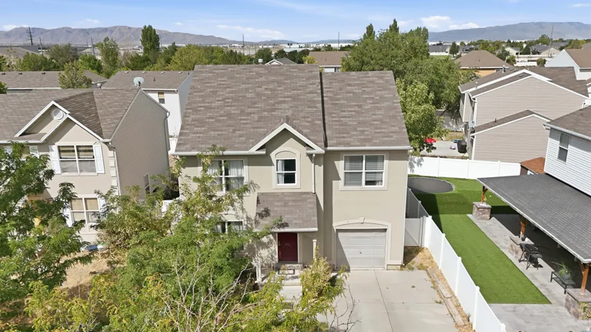 Stucco exterior residence featuring an attached garage, paved driveway, and covered patio with stone pillar accents