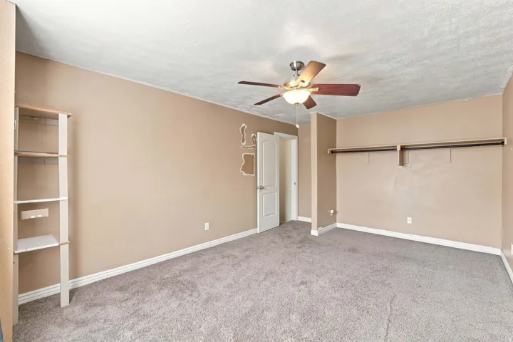 Built-in shelving unit, ceiling fan with integrated lighting, built-in closet storage, light-colored carpeting, and a white interior door
