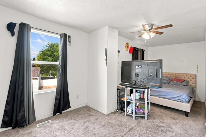 White painted walls, textured ceiling, window with exterior scenery, carpeted flooring, and a ceiling fan with integrated lighting