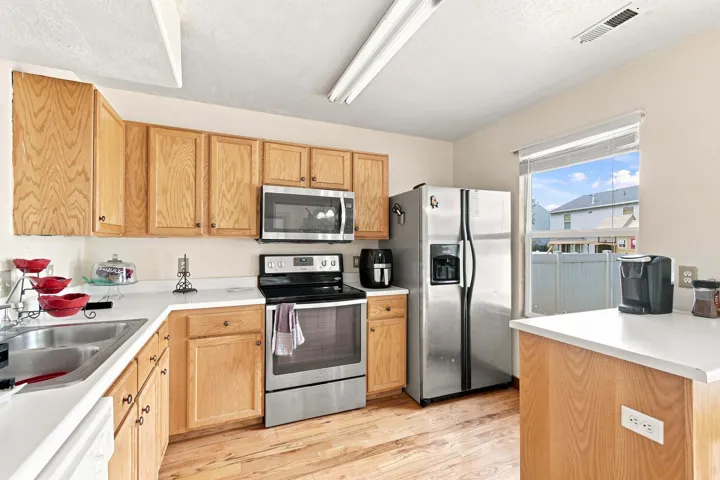 Kitchen featuring wood-finish flooring, light wood cabinetry, white countertops, stainless steel appliances, and a window for natural light