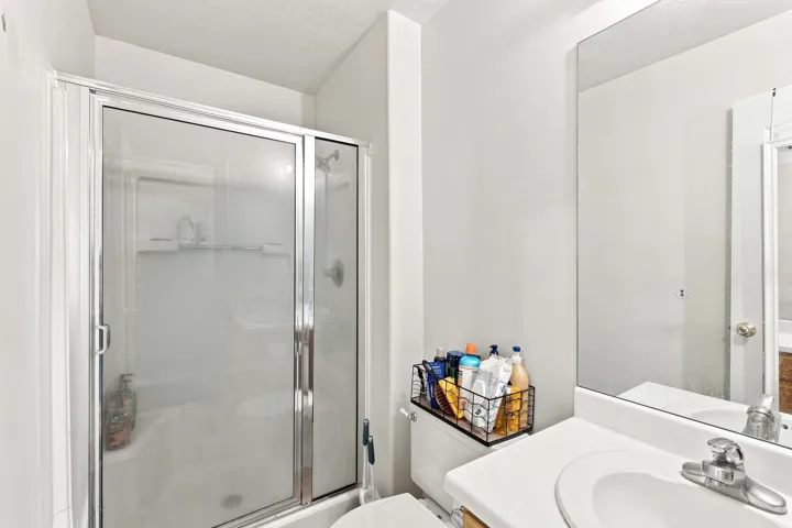 Shower with glass enclosure, white vanity, integrated sink, chrome faucet, and frameless wall mirror