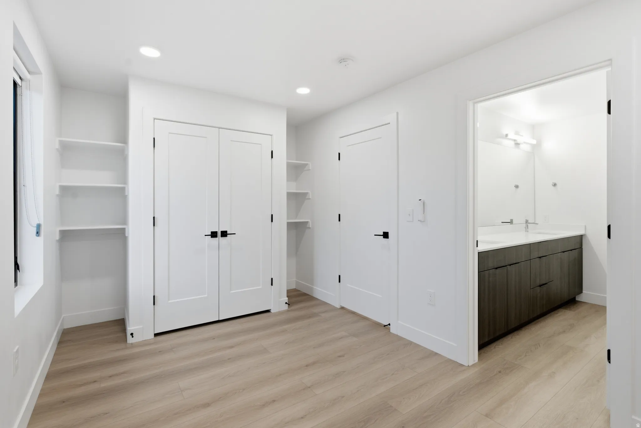 LVP flooring, recessed ceiling lighting, built-in shelving, white double doors, and an attached bathroom with a dual vanity