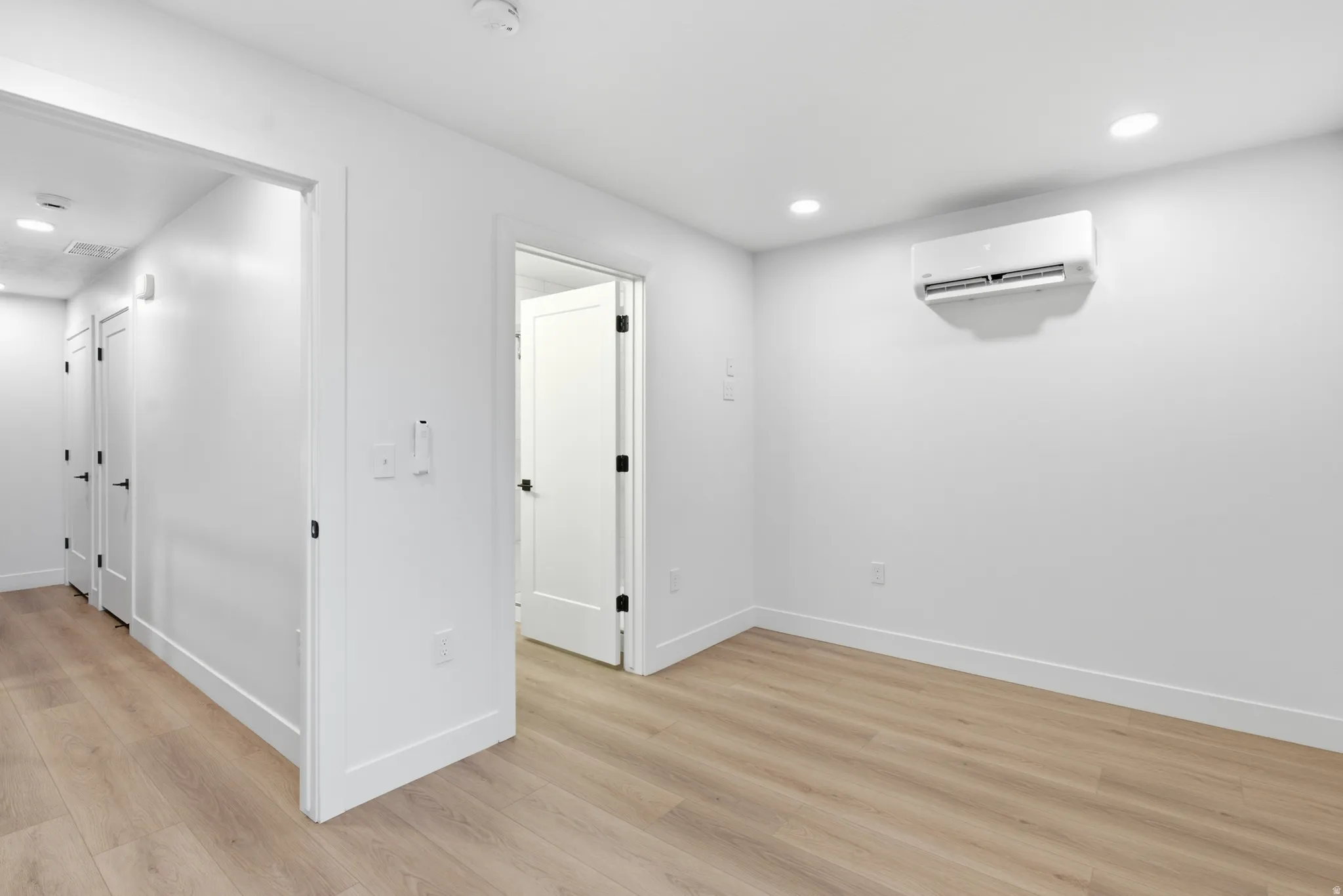 Neutral color palette with LVP flooring, recessed lighting, and a wall-mounted air conditioning unit