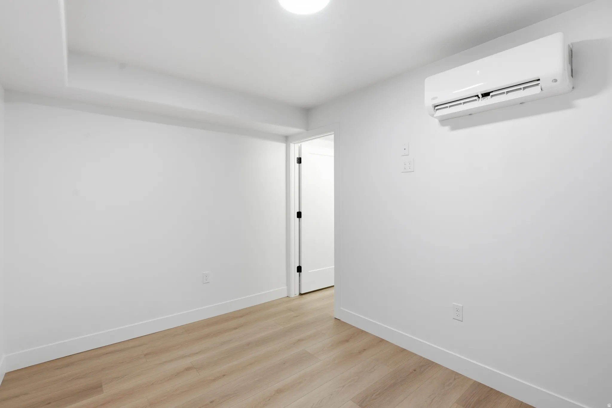 Recessed lighting, LVP flooring, white walls, mini-split air conditioning unit, and a white door with black hardware