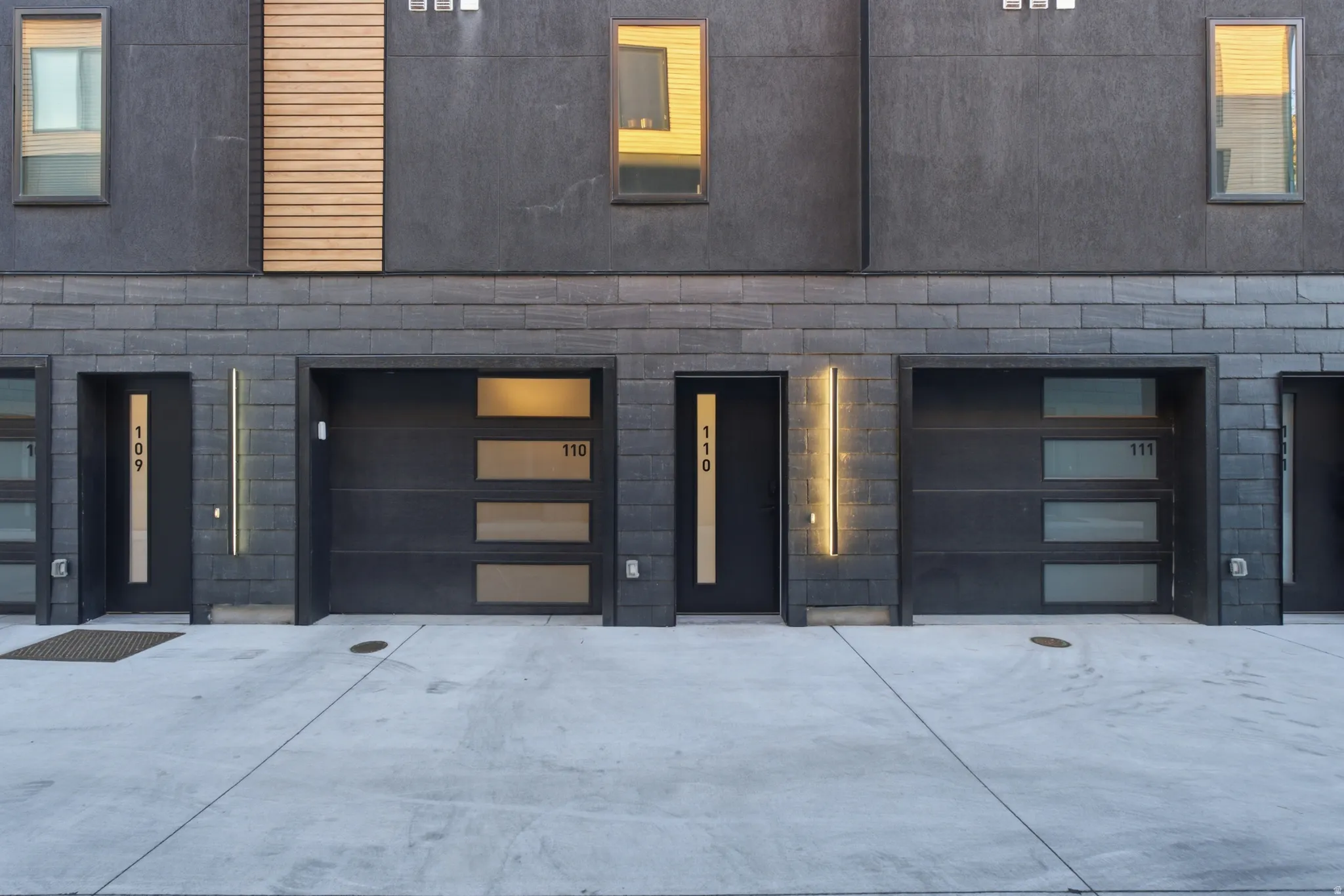 Modern facade featuring dark siding, brick accents, wood-finish paneling, and contemporary garage doors with frosted glass panels