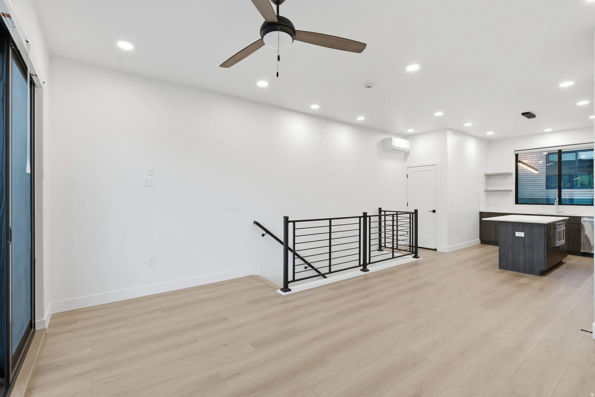 Recessed lighting illuminates the open living area featuring LVP flooring, a contemporary ceiling fan, and a modern metal railing