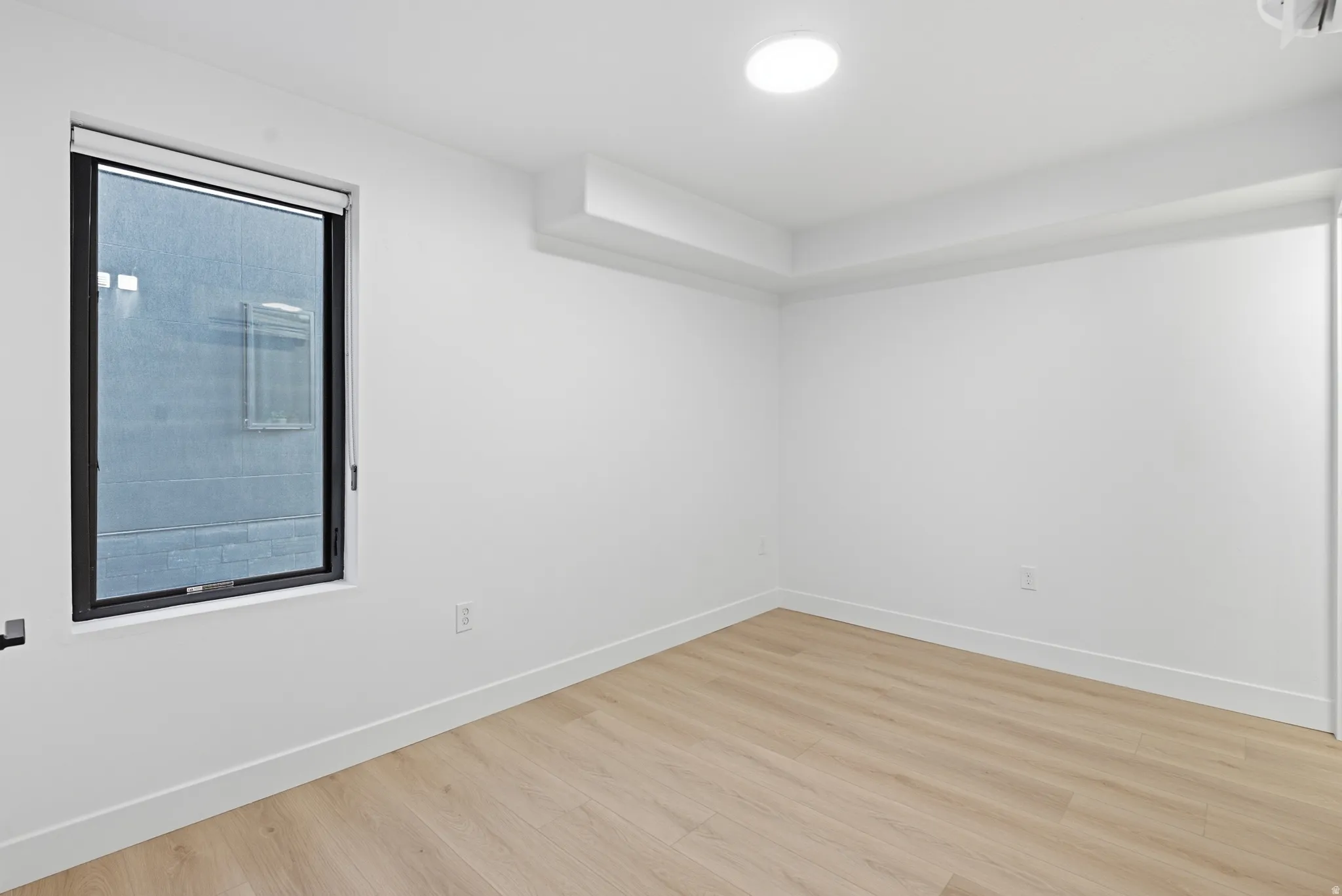 Recessed ceiling light, LVP flooring, white walls, and a window with a roller shade