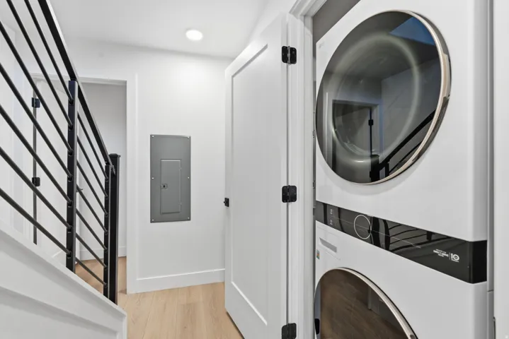 Stacked washer and dryer unit, wood-finish flooring, modern black metal stair railing, recessed ceiling lighting, white interior door with black hardware