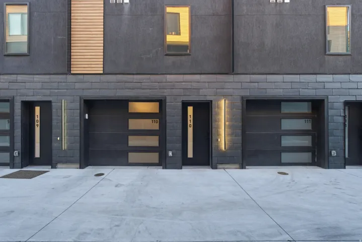 Modern facade featuring dark siding, brick accents, wood-finish paneling, and contemporary garage doors with frosted glass panels