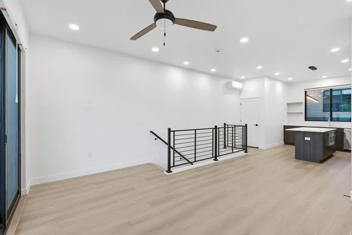 Recessed lighting illuminates the open living area featuring LVP flooring, a contemporary ceiling fan, and a modern metal railing
