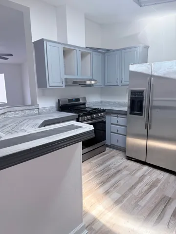Wood-finish flooring, stainless steel appliances, light blue cabinetry, tiled backsplash, and multi-tone countertops