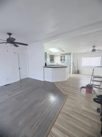 Open-concept living space with wood-finish flooring, a kitchen featuring light cabinetry and a skylight, and ceiling fans