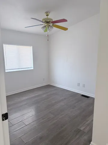 Wood-finish flooring with white baseboards, bright white walls, and a window with blinds