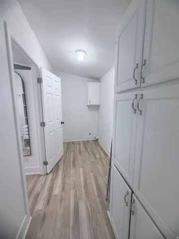Hallway featuring wood-finish flooring, white panel doors, recessed wall cabinet, and built-in white cabinetry with silver-tone hardware