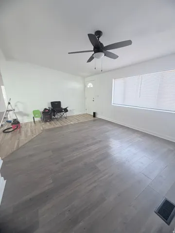 Spacious room featuring wood-finish flooring, a contemporary ceiling fan with integrated lighting, and a white entry door with a decorative glass insert