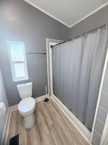 Full bathroom featuring a single window, white toilet, wood-finish flooring, and a shower with gray subway tile surround