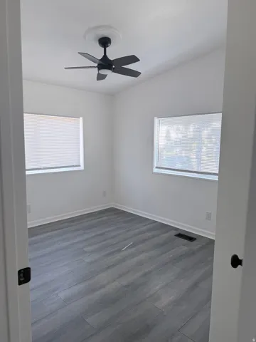 Wood-finish flooring, white walls, two windows with blinds, and a ceiling fan with light fixture